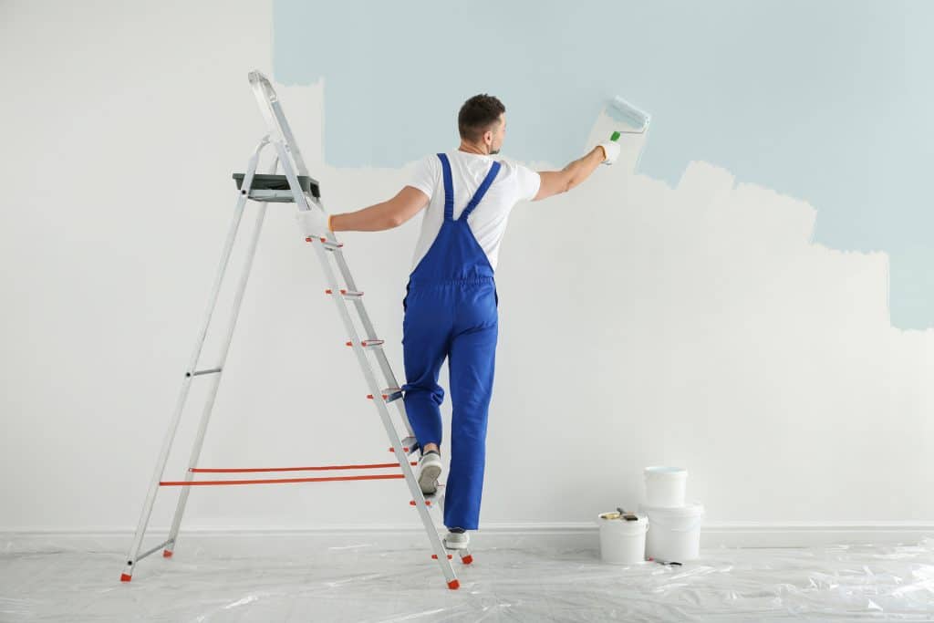 painter using roller to paint wall light blue